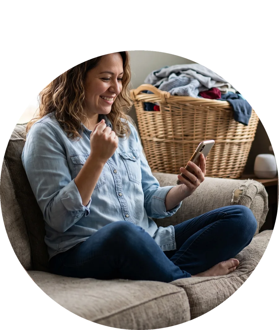 A happy woman on her sofa celebrating while looking at her phone